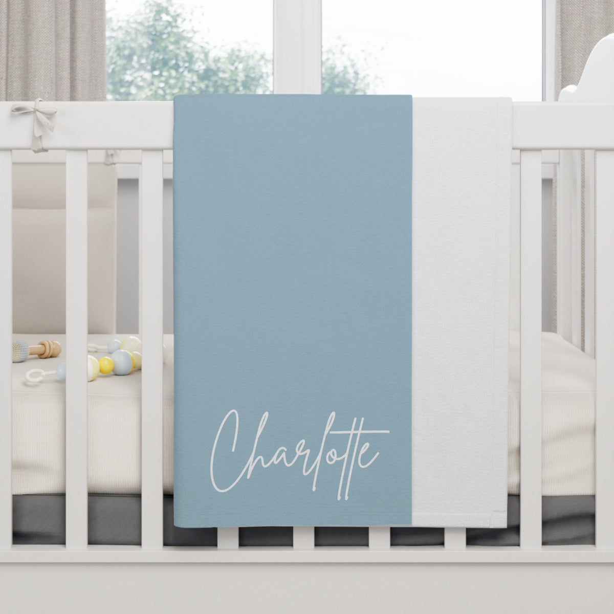 Blue blanket with 'Charlotte' printed on it draped over a crib.
