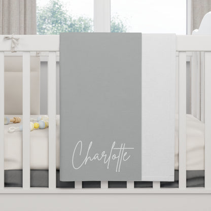 Gray blanket with 'Charlotte' printed on it draped over a crib.