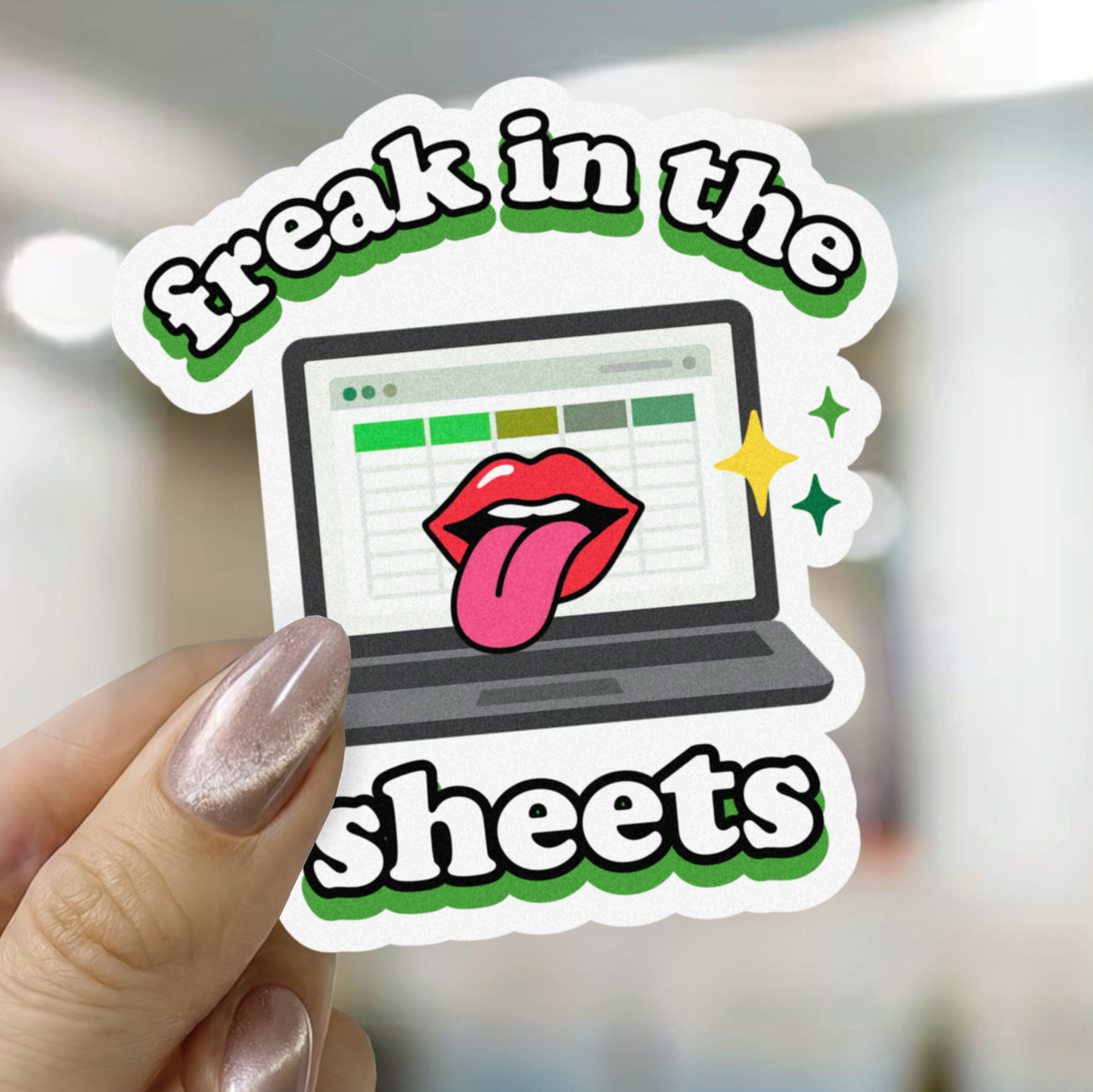Sticker with laptop and lips design held by a hand, text 'freak in the sheets' on a blurred background