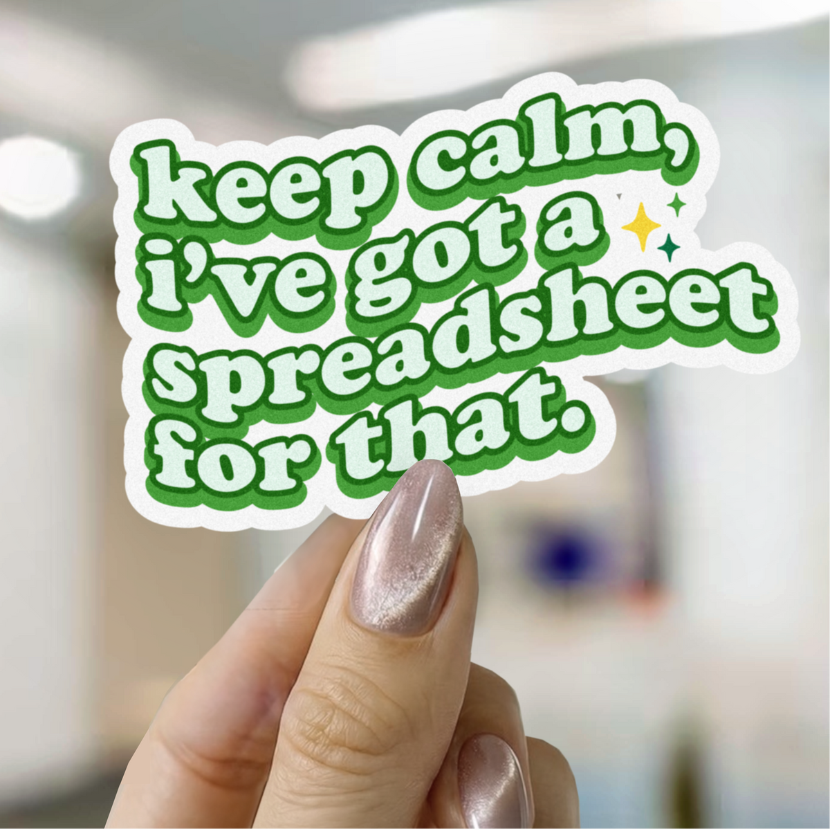 Hand holding a sticker with text 'keep calm, I've got a spreadsheet for that.' against a blurred indoor background.
